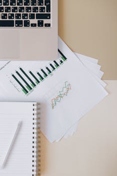 Flat lay of a workspace featuring a laptop, graphs, and a notebook for financial analysis.
